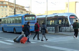Viaggiatori con i trolley davanti a un bus e alla tramvia di Firenze