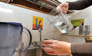 acqua versata da una caraffa nel bicchiere e più indietro un rubinetto di cucina