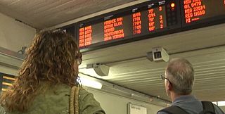 persone controllano il tabellone degli orari del treno