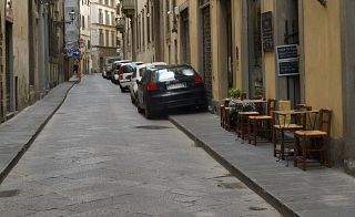 In foto un marciapiede con le sedie, invaso dalle auto in sosta 