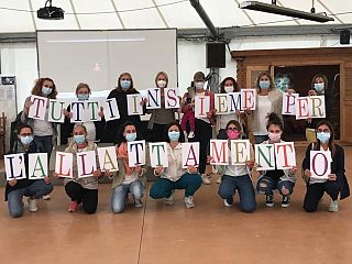 Foto di gruppo, ognuna mostra una lettera a comporre la scritta "Tutti insieme per l'allattamento"